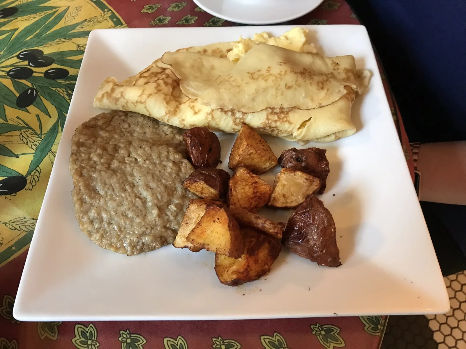 A breakfast plate of a folded crepe, grits and roasted potatoes at a restaurant in West Palm Beach.