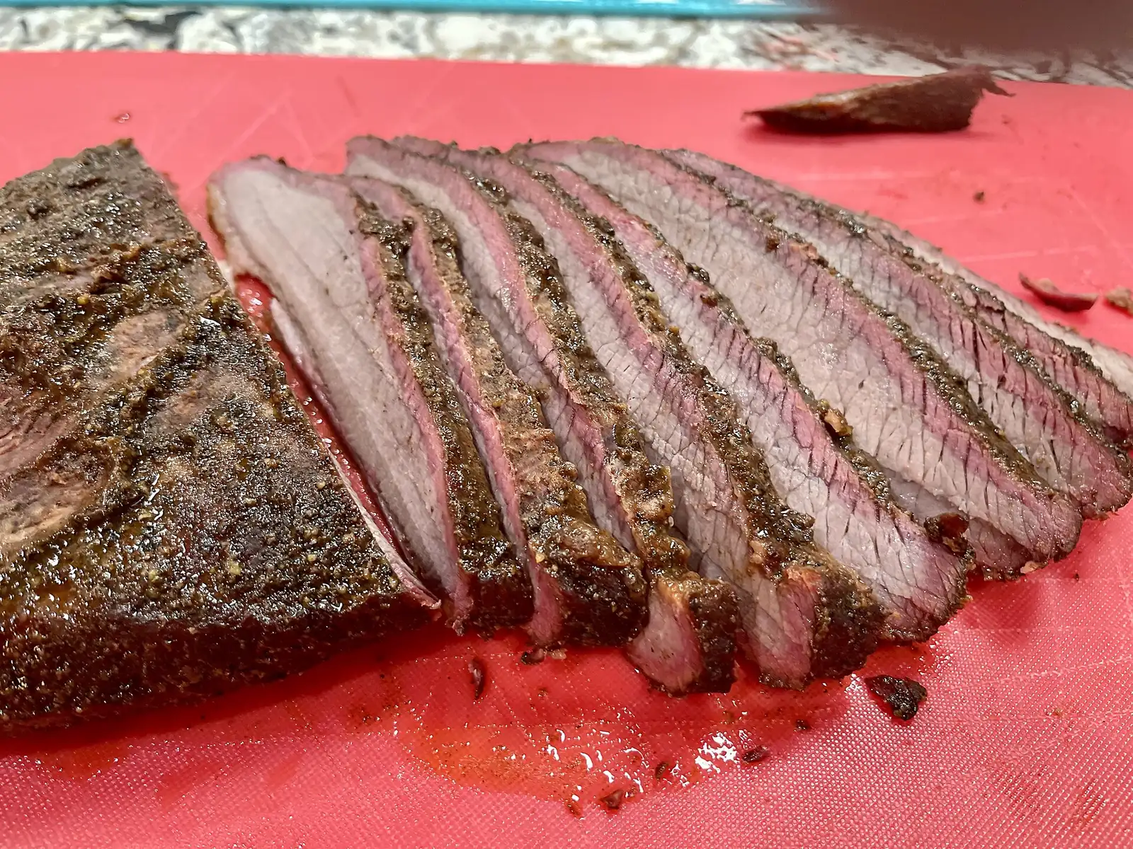 Sliced smoked brisket on a cutting board, showing the pink smoke ring under the bark.